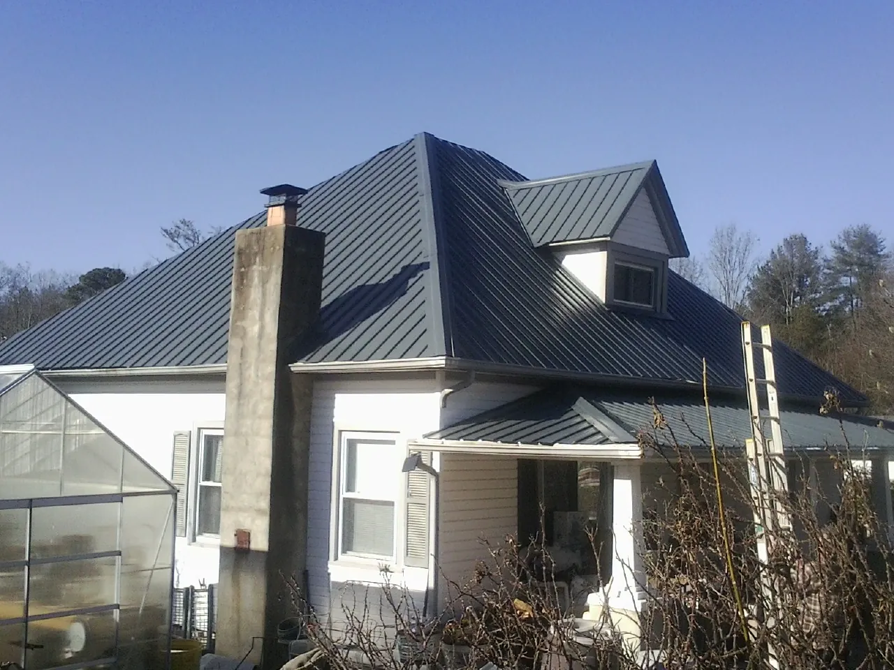 Dark blue standing seam metal roof on a white farmhouse with dormer — Slate & Tile Roof Repair by Roofing Brothers in Spring Hope
