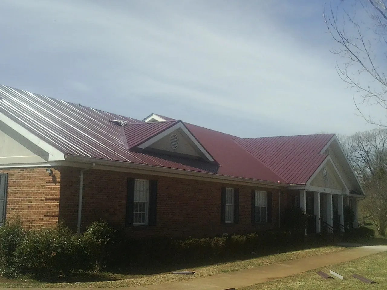 Red metal roof with gabled entries on a long brick building, from a Hail Damage Roof Repair job in Spring Hope