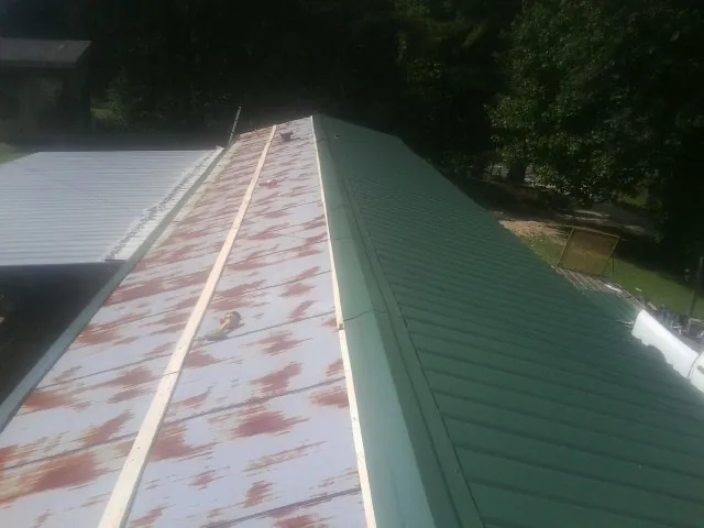 Old rusted panels beside newly installed green metal roofing — Wind Damage Roof Repair by Roofing Brothers in Spring Hope
