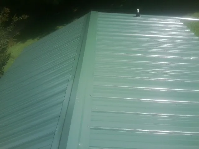 New green metal panels meeting at the ridge of a roof — Flat Roof Repair work by our crew in Spring Hope
