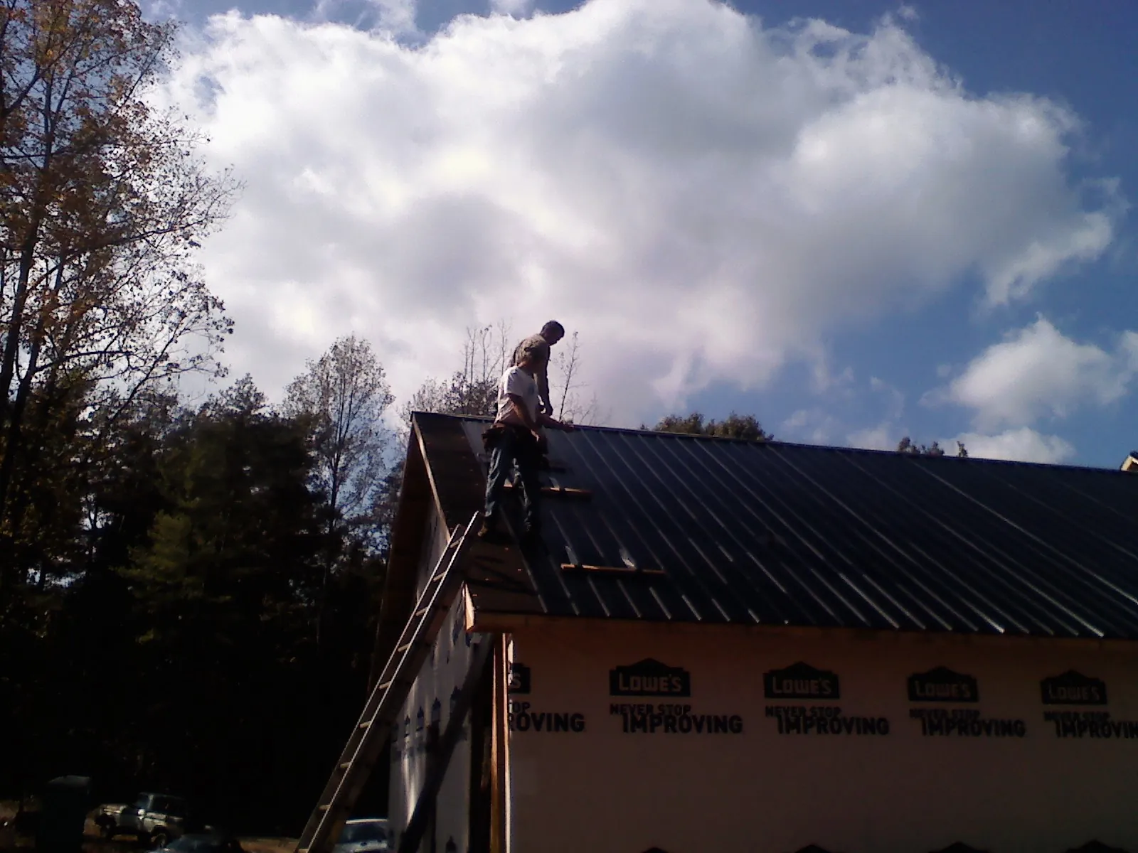 Roofer fastening dark metal panels high against a cloudy sky, from a Roof Inspection job in Spring Hope